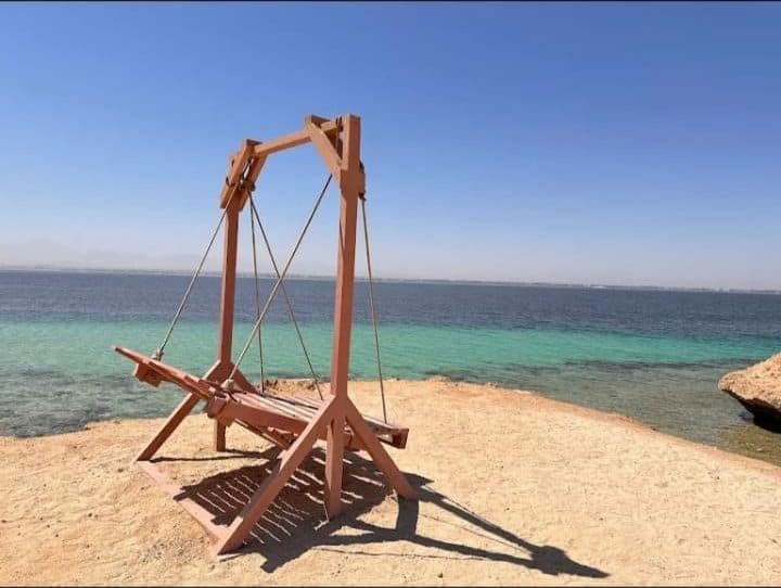 Wooden beach swing standing on the sand at the edge of the sea with turquoise water and clear sky behind it